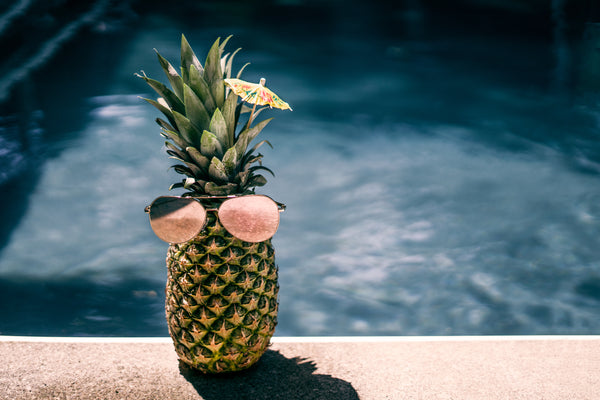Pineapple with pink lens aviator sunglasses placed on top at edge of pool